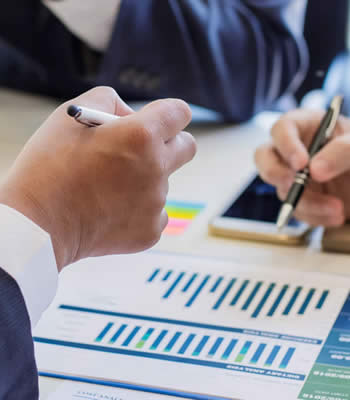 hands holding pens on top of financial charts